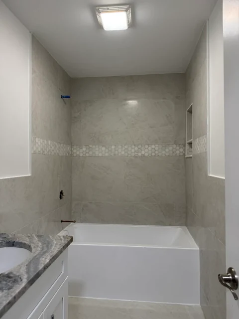 Bathtub surround with neutral wall tile and a horizontal mosaic tile detail