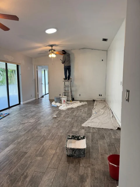 Interior painting in progress in a room with protected flooring and a vaulted ceiling