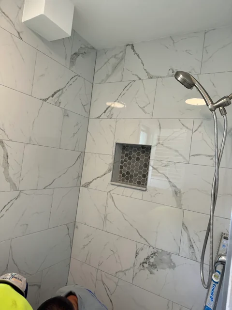 Shower renovation with marble-look wall tile, handheld shower, and a recessed niche