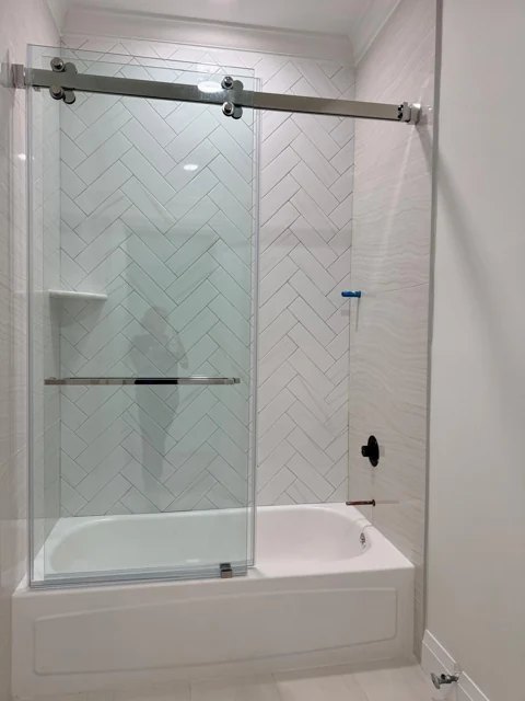 Bathtub with a sliding glass shower door and white herringbone wall tile